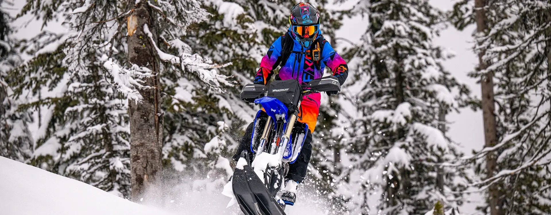 Snow Bike Rider in Colorful Gear Riding Through Snow Covered Forest Terrain